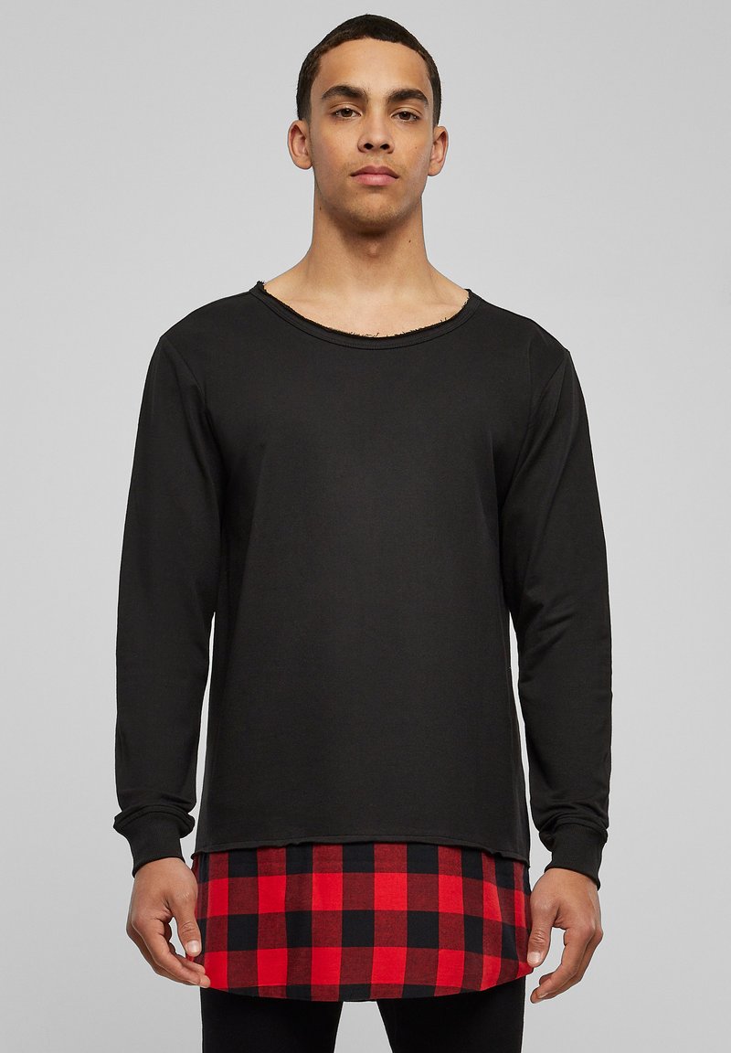 T-shirt noir à manches longues avec un col usé, superposé sur une chemise en flanelle à carreaux rouges et noirs, avec un ourlet arrondi.