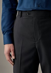 Pantaloni neri con una texture liscia, dotati di chiusura con bottone e tasche laterali, abbinati a una camicia blu a maniche lunghe con una texture.