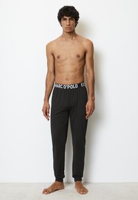 Svarta joggingsbyxor i mjukt material med elastiskt midjeband som har "MARC O'POLO"-logotypen i vitt. Tajt vid vristerna.