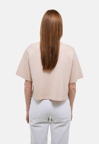 Haut court à manches courtes en coton rose clair, avec une coupe décontractée et un col rond. Un jean blanc complète le look.