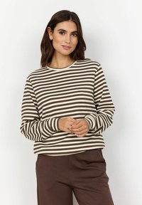T-shirt à manches longues rayé en crème et marron, avec un col rond et une coupe décontractée, présentant une subtile texture côtelée. Associé à un pantalon marron.