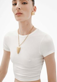 Top corto de canalé blanco con mangas cortas, combinado con un collar de cadena dorada con un colgante en forma de gota y grandes pendientes cuadrados dorados.