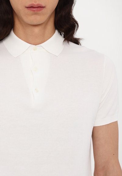 Hvid kortærmet polo shirt lavet af blødt stof med en smal krave og en tre-knap lukning, der har en subtil struktur over det hele.