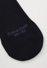 Calcetín de algodón negro con textura suave, con la marca blanca "Calvin Klein" y las indicaciones de tamaño (39-42) impresas en el lado.