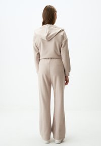 Lichtbeige hoodie en bijpassende wijduitlopende broek gemaakt van zachte stof. Voorzien van een capuchon en een elastische tailleband voor comfort.