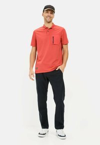 Rød polo t-shirt med korte ærmer og en forlomma, parret med mørke bukser og hvide sneakers. Afslappet design og løs pasform.