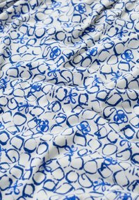 Katoenen stof met een witte achtergrond met een herhalend blauw cirkelvormig en abstract patroon. Zachte textuur, licht gekreukelde uitstraling.