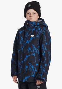 Blå och svart mönstrad jacka med huva, tillverkad av vattentätt material, med dragkedja och logotyp på bröstet, designad för kallt väder.