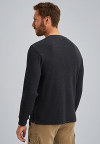 Dunkelgraues Langarmshirt mit gerippter Textur, runden Ausschnitt und einem kleinen Akzentknopf auf der Rückseite; gezeigt an einem männlichen Modell.