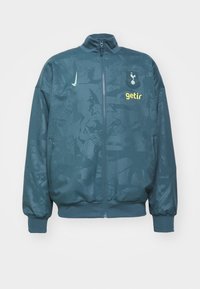 Giacca in teal con zip, caratterizzata da un motivo testurizzato, con un logo e la scritta "getir" in giallo. I polsini e l'orlo a costine assicurano una vestibilità aderente.
