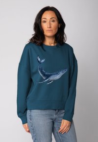 Sweatshirt turquoise en tissu doux avec un graphique de baleine en bleu et blanc sur le devant. Coupe décontractée avec des poignets et un ourlet côtelés.