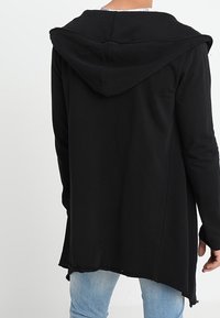 Sudadera negra con capucha, con un dobladillo asimétrico y mangas largas, fabricada en un tejido suave, con un diseño simple sin cierres visibles.