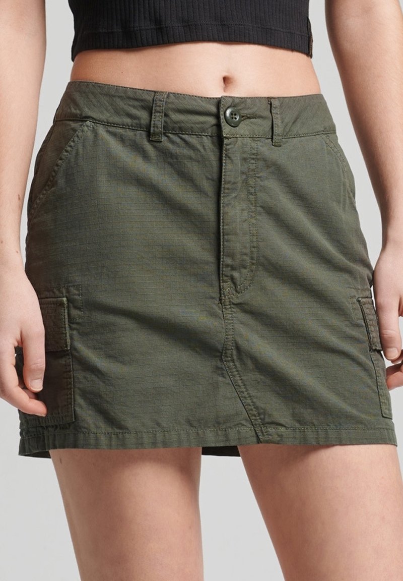 Khaki-väri cargo-hame, jossa on keskikorkeus vyötärö, napitus, kaksi sivutaskua ja teksturoitu kangas. Pituus ulottuu puoliväliin reisiä.