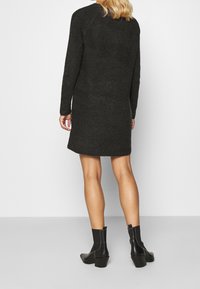 Robe en maille côtelée gris foncé, manches longues, longueur au genou, silhouette droite. Portée avec des bottines noires.