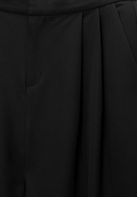 Černé kalhoty vyrobené z měkké tkaniny, zakončené sklady, se strukturovaným designem a předními kapsami, které ukazují hladkou, matnou texturu.