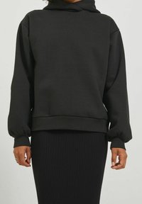 Svart huvtröja med lös passform, ribbade ärmslut och midja. Tillverkad av mjukt tyg med en slät yta. Minimalistisk design.