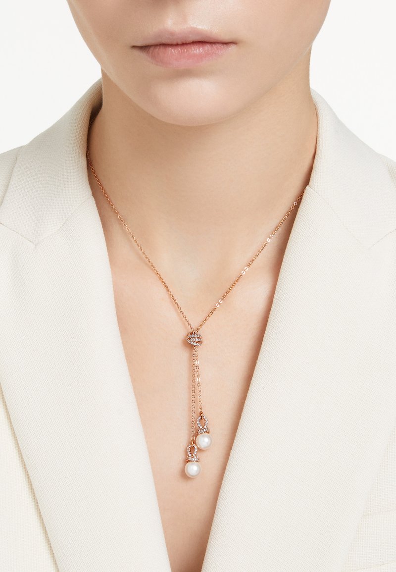 Collar de oro rosado, con una delicada cadena, detalle de cristal redondo y dos perlas blancas en los extremos. Diseño simple y elegante.