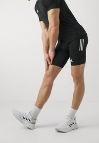 Camisa atlética negra y pantalones cortos con tres rayas blancas, combinados con zapatillas blancas. La tela parece elástica y ajustada.