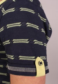 Laivaston sininen lyhythihainen paita, jossa on teksturoitu kangas ja keltavihreä raitakuosi, sekä käänteet, jotka on kiinnitetty keltaisella napilla.