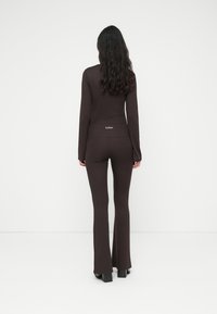 Καφέ μπλούζα με μακριά μανίκια και εφαρμοστά παντελόνια με φαρδύ τελείωμα, και τα δύο από λείο, ελαστικό ύφασμα. Τα παντελόνια έχουν διακριτικό λογότυπο στο πίσω μέρος.