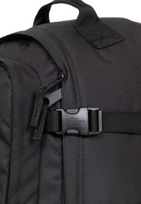 Mochila negra con un tejido texturizado, herrajes de plástico, tiradores de cremallera y una correa de hebilla en la solapa para un cierre seguro.