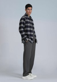 Marineblauwe en witte geblokte flanellen shirt met zwarte knopen, gecombineerd met grijze broeken en witte sneakers. Textuurstof met een ontspannen pasvorm.
