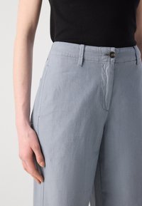 Light blue, high-waisted trousers made of soft fabric. Features a button closure, two side pockets, and subtle texture.