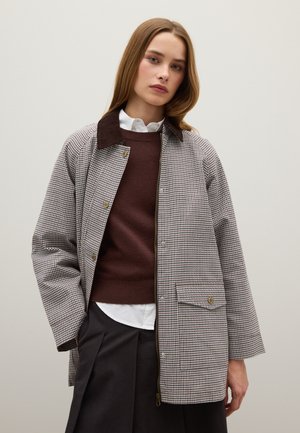 Houndstooth-gepatrooneerde jas in bruin en crème, met een donkerbruin corduroy kraag, een voorzak en gouden drukknoopsluitingen.