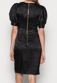 Black dress with puff sleeves, textured leopard print. Features a central gold zipper running vertically at the back. Smooth satin material.
