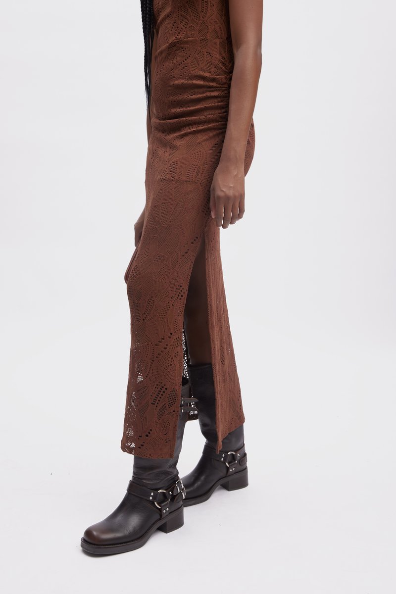 Brązowa koronkowa sukienka o dopasowanym kroju, z kwiatowymi wzorami i bocznym rozcięciem, zestawiona z czarnymi skórzanymi botkami za kostkę ze srebrnymi akcentami.