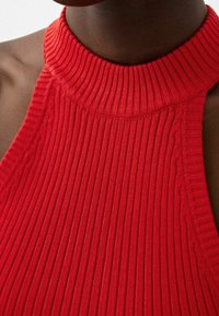 Top a halter rosso a costine con collo alto. Il tessuto è texturizzato con strisce verticali, evidenziando un design aderente e senza cuciture nelle ascelle.