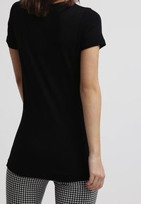 Kvinna i en enkel svart kortärmad tröja och byxor med svart-vitt hundtandmönster, visad bakifrån.