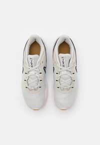 Light grey athletic shoes with a textured honeycomb pattern, rounded shape, flat laces, and tan inner lining. Accented with black logo details.