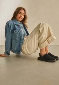Denim takki nappilukolla, vaaleansininen väri, yhdistettynä kermanvärisiin leveälahkeisiin housuihin ja mustiin nilkkureihin, joissa on solkikoristus.