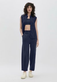 Marineblaue Fleece-Weste mit Stehkragen, kombiniert mit passenden weiten Hosen. Das Outfit hat eine strukturierte Oberfläche und wird durch cremefarbene Sneaker ergänzt.