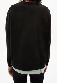 Czarny, oversize sweatshirt z szerokim dekoltem i długimi rękawami, z kontrastowym jasnoniebieskim wykończeniem widocznym na dole. Gładka, miękka tekstura.