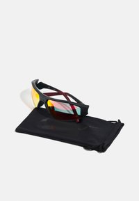 Occhiali da sole sportivi con montatura nera, lenti gialle e rosa, poggiati su un sacchetto morbido nero. Le lenti hanno una finitura riflettente.