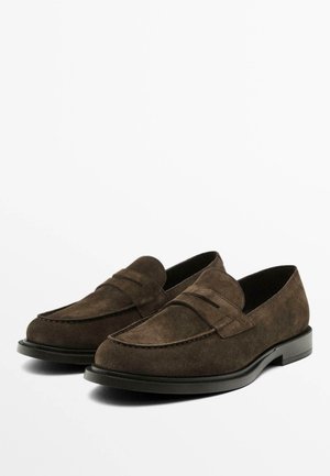 Une paire de mocassins en daim brun foncé avec des semelles noires, présentant un détail classique de bandeau façon penny, présentée sur un fond blanc.