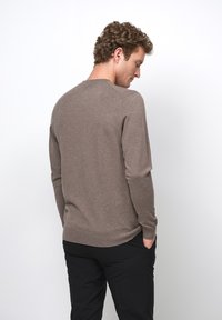 Pull in maglia marrone con collo rotondo, maniche lunghe e polsini a costine. Texture liscia, design aderente, vista che mostra i dettagli della schiena e delle spalle.