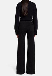 Pantalones vaqueros de pierna ancha en negro, hechos de denim, con bolsillos traseros y una cinturilla, combinados con un suéter negro de canalé.