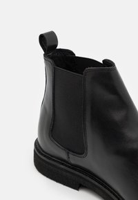 Bottine Chelsea en cuir noir avec panneaux latéraux élastiques, bout arrondi et languette de tirage. Dotée d'une semelle en caoutchouc texturée et d'une finition élégante et lisse.