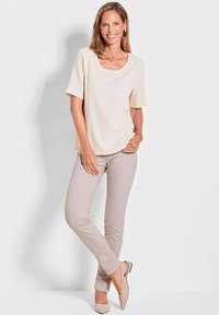 Licht beige kort mouwtop met een ronde hals en ribbeltextuur, gecombineerd met lichtgrijze slim-fit broek en beige puntige schoenen.