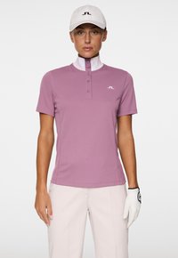 Rosa Golf-Polo mit kurzen Ärmeln, hohem Kragen, einer Knopfleiste mit vier Knöpfen und einem kleinen Logo auf der Brust. Glatte Textur, entworfen für aktiven Einsatz.