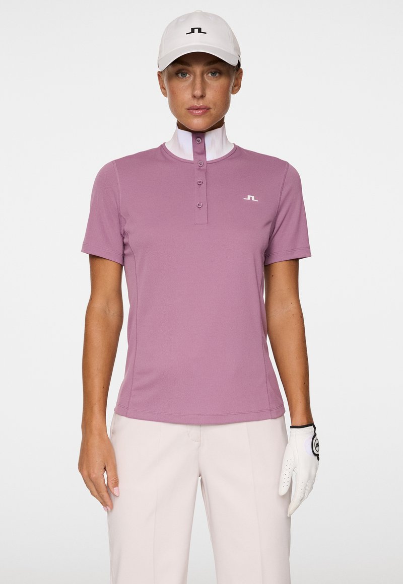 Rosa Golf-Polo mit kurzen Ärmeln, hohem Kragen, einer Knopfleiste mit vier Knöpfen und einem kleinen Logo auf der Brust. Glatte Textur, entworfen für aktiven Einsatz.