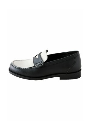 Mocassins en cuir noir avec un accent blanc et gris, présentant un détail de couture surélevé et une semelle plate en caoutchouc, présentés de côté.