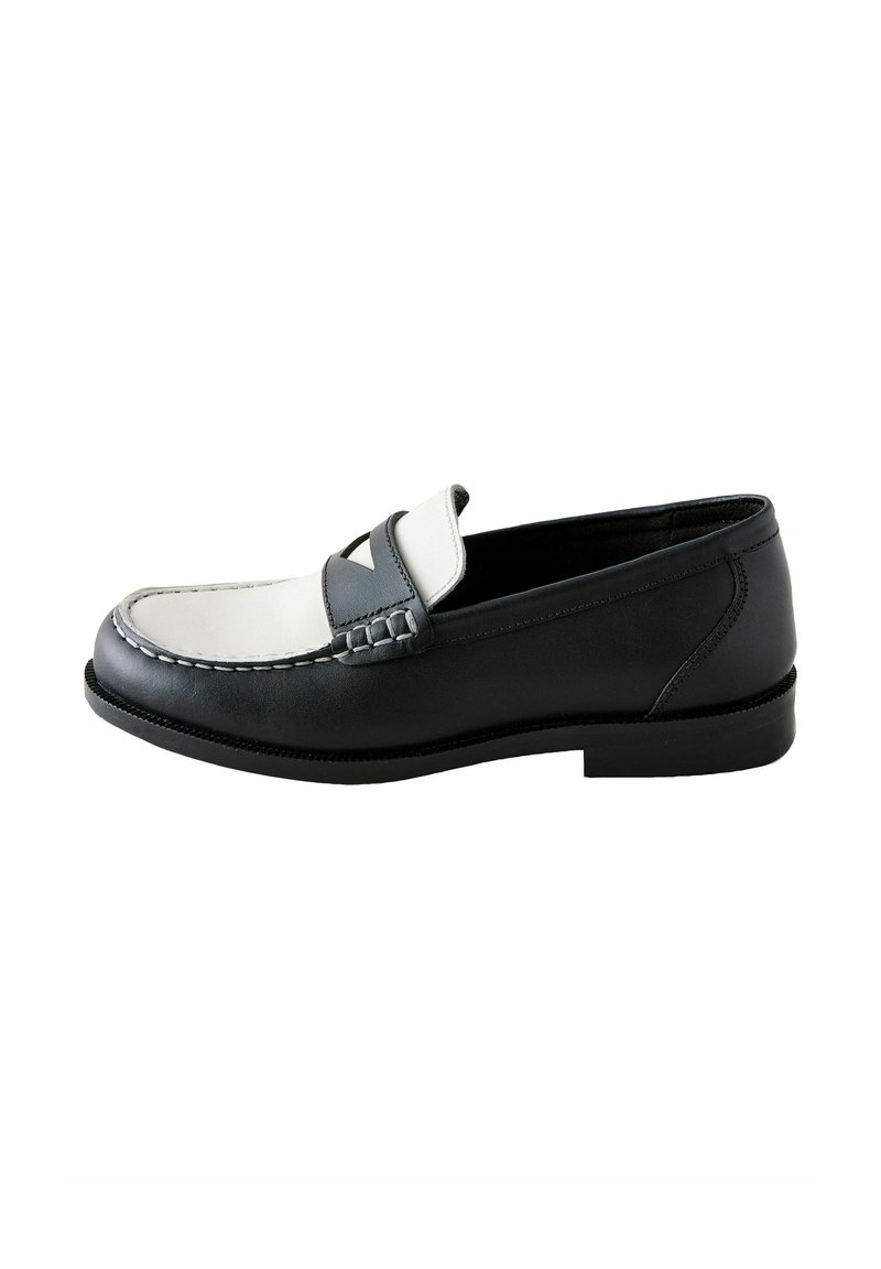 Mocassins en cuir noir avec un accent blanc et gris, présentant un détail de couture surélevé et une semelle plate en caoutchouc, présentés de côté.
