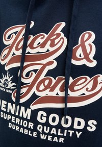 Marineblaue Stoff mit braunem und weißem "Jack & Jones"-Logo, Sonnengrafik und dem Text "Denim Goods Superior Quality Durable Wear".