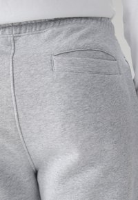 Heledate hallide dressipükste lähivaade, kus on nähtav õmmeldud tagatasku ja valge särk pael üleval.