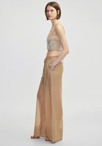 Koronkowy top z koralikami o wzorzystym designie i cienkimi ramiączkami, zestawiony z lekkimi, wysokimi, półprzezroczystymi beżowymi spodniami z elastycznym pasem.