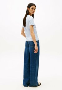 T-shirt di cotone azzurro abbinato a jeans in denim scuri a gamba larga e vita alta. Il modello si trova di fronte a uno sfondo neutro.